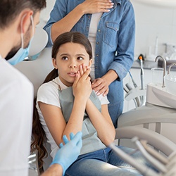 Girl in dental chair looking at dentist holding hands to face