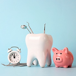 Clock next to large tooth holding dental instruments and pink piggy bank