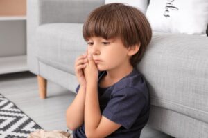 little boy sitting by the couch holding his face in pain