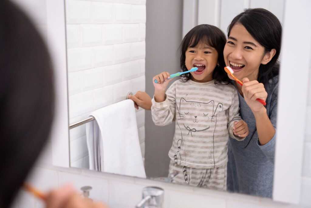 Woman and small girl brushing teeth together at the bathroom mirror